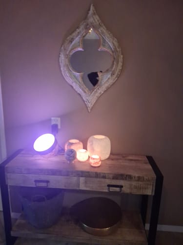 Recensent toont de mangohouten sidetable tegen een muur, sfeervol gedecoreerd met kaarsen en een lamp.