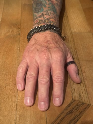 Customer's hand showing the dark metal Connected at the Cross link bracelet worn on a tattooed wrist.
