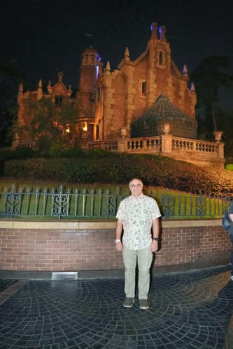 Reviewer wearing the Mickey's Christmas Carol shirt in front of a large, lit mansion at night.