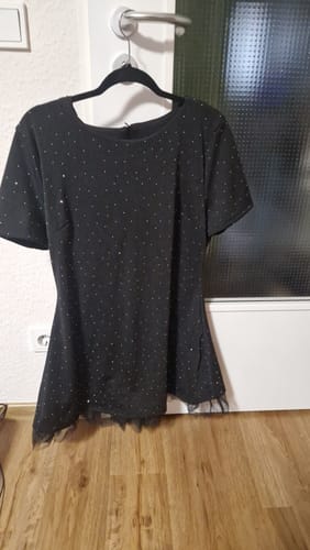 Rezensent zeigt das elegante schwarze Kleid mit schimmernden Details und Netz-Saum auf einem Bügel.