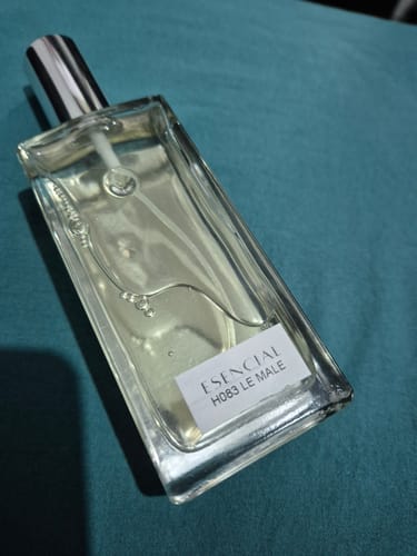Cliente muestra el frasco de perfume Esencial H083 Le Male casi lleno sobre una superficie azul.