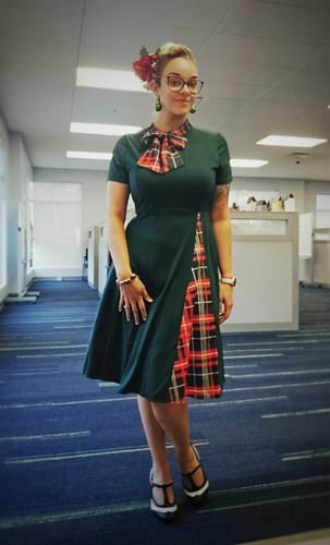 Reviewer in an office wearing the green swing dress with a plaid bow and patchwork panel.
