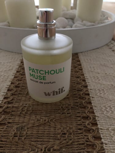 Customer's frosted glass bottle of Patchouli Muse perfume on a woven placemat.