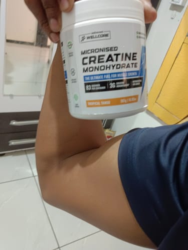 Reviewer holding a tub of Wellcore Creatine Monohydrate and flexing their bicep.