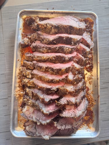 Un cliente muestra su Rib Eye Pieza Básica cocido y rebanado sobre una charola para hornear.