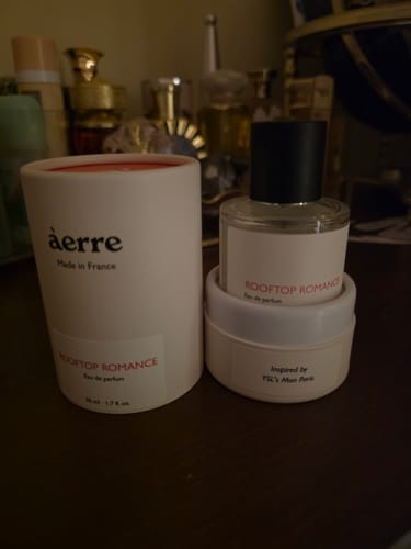 Customer's Rooftop Romance perfume bottle and its white cylindrical packaging on a dark surface.