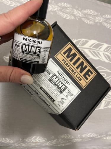 Cliente tiene in mano la boccetta del profumo PATCHOULI di fronte alla sua scatola nera.