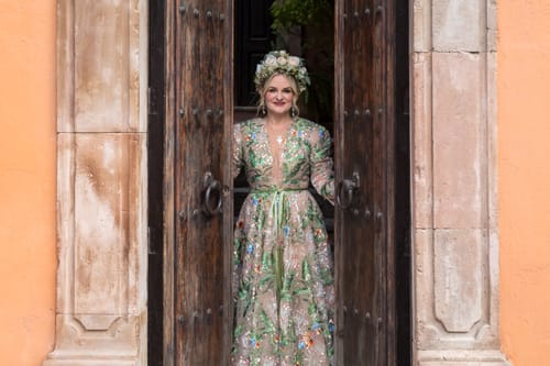 Reviewer wearing the embroidered Whispering Forest Gown with a cinched waist, standing in a large wooden doorway.
