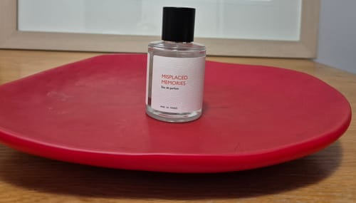 Customer's Misplaced Memories perfume bottle resting on a bright red, decorative tray on a wooden table.