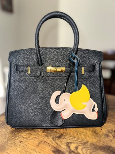 Reviewer's black pebbled Warkin 25 bag sitting on a wooden table with a decorative elephant charm hanging from the handle.