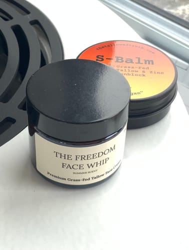 Customer's small, dark jar of The Freedom Face Whip cream on a white surface next to another product.