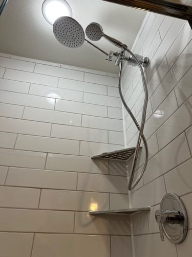 Reviewer's chrome shower filter installed on a wall with a dual shower head in a white tiled shower.