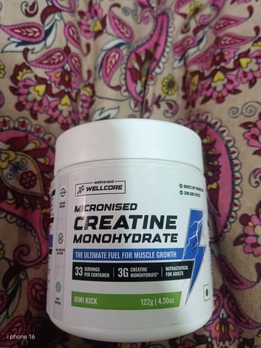 A customer's white tub of Wellcore Micronised Creatine Monohydrate in the Kiwi Kick flavor, set against a patterned background.