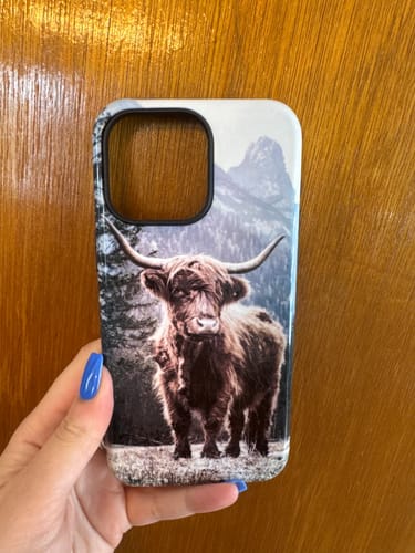 Customer holding a custom iPhone 15 Pro Max case with a detailed print of a Highland cow in a mountain landscape.