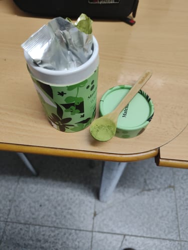 Cliente mostrando la cuchara de bambú del Kit Imprescindible con polvo de matcha sobre la tapa del envase.