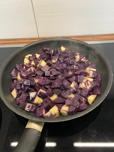 Rezensent brät gewürfelte, lila Kartoffeln 'Purple Rain' in einer Pfanne.