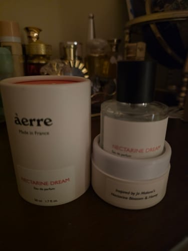 Customer's Nectarine Dream perfume bottle and its white cylindrical packaging on a dark wooden surface.