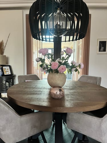 Recensent's boeket roze zijden pioenrozen in een grote vaas op een houten eettafel.