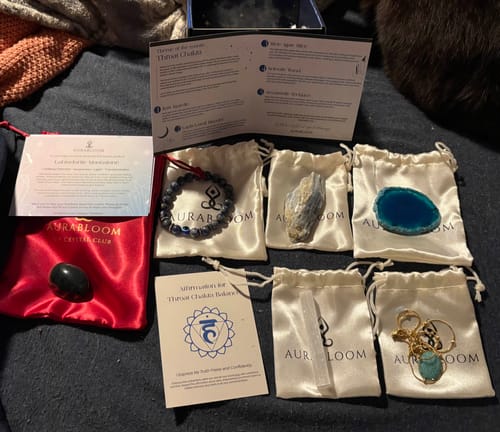 Customer's AuraBloom Subscription Box contents for the Throat Chakra laid out, showing crystals, pouches, and a necklace.