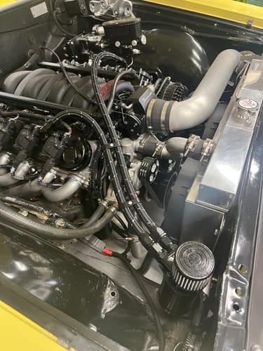 Reviewer's black Billet Oil Catch Can installed in a car's engine bay, connected with dual braided hoses.