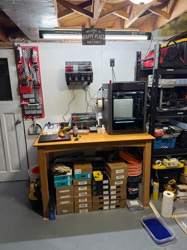 Reviewer's two Bambu Lab AMS 2 Pro units set up with a 3D printer on a wooden desk in a workshop.