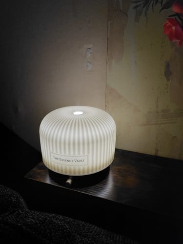 Reviewer's white Ceramic Electric Diffuser illuminated on a dark wood shelf.