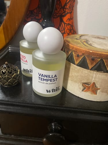 Customer's bottle of Vanilla Tempest perfume sits on a dark dresser in front of another perfume bottle.