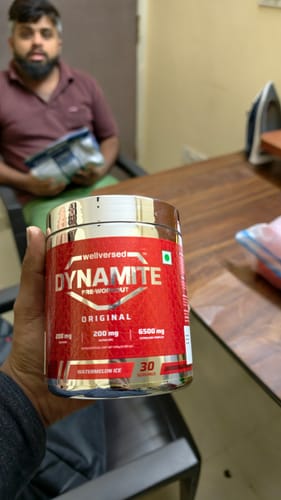 Reviewer holds up a red container of Dynamite Pre-Workout in Watermelon Ice flavor.