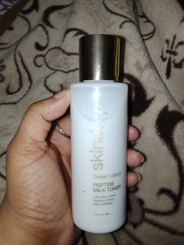 Customer holding the white bottle of DREAM GLAZE - Peptide Milk Toner, which has a gold cap.