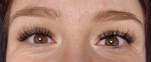 Kundin zeigt lächelnd ihre langen, vollen Wimpern aus dem persönlichen Starter Kit in einer Nahaufnahme.