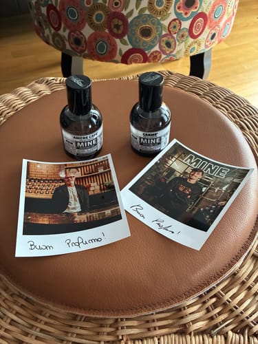 Due flaconi del profumo CARME' del recensore, su un pouf marrone con due foto istantanee.