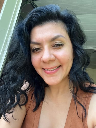 Reviewer with dark wavy hair smiling, showing radiant skin after using Grass Fed Tallow & Honey Balm.
