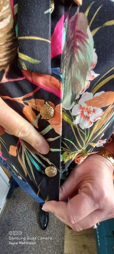Close-up: Reviewer pointing to gold buttons on a shirt made from the Floral Escape Viscose Challis Fabric.