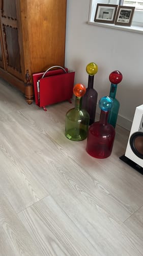 Recensent toont de POLSPOTTEN Bubbles & Bottles set van 4 kleurrijke karaffen op een lichte vloer.