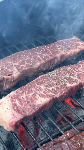 Cliente asando dos tablitas de lomo crudas y sazonadas sobre una parrilla con brasas calientes.