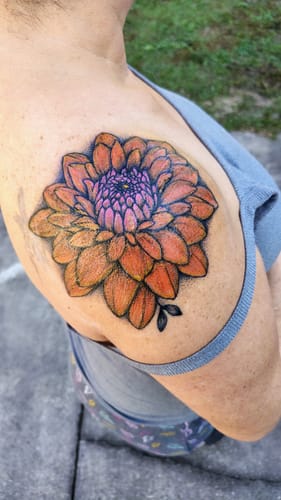 Reviewer shows their finished, colorful flower tattoo on their shoulder, done painlessly using the reviewed numbing cream.