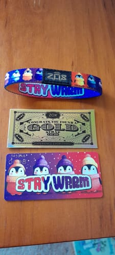 Customer's Stay Warm Bracelet, a matching card with penguins, and a special gold card displayed on a wooden surface.