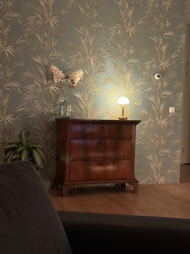 Recensent toont de gouden Humble Bug tafellamp ingeschakeld op een houten dressoir.