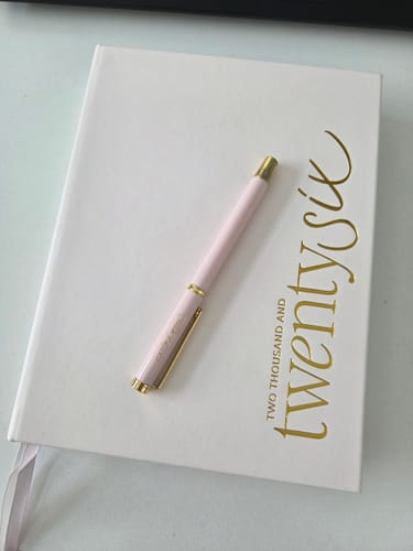 Customer's 2026 Essential Planner with a white cover and gold text. A pink pen is resting on top.