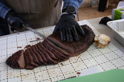 Reviewer slicing a large, smoked USDA Prime Brisket with a dark bark on a cutting mat.