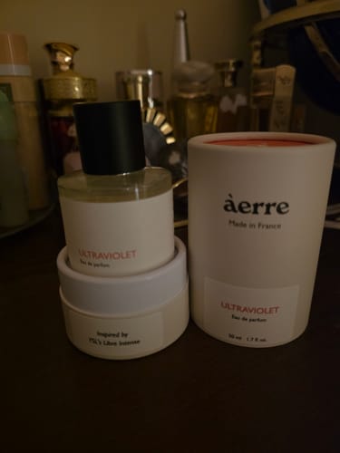 Customer's Ultraviolet perfume bottle and its white cylindrical packaging on a dark surface.