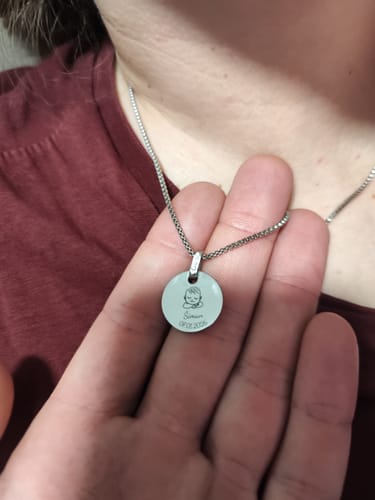 Reviewer holds up the engraved silver-tone pendant of their Stellar Newborn necklace.