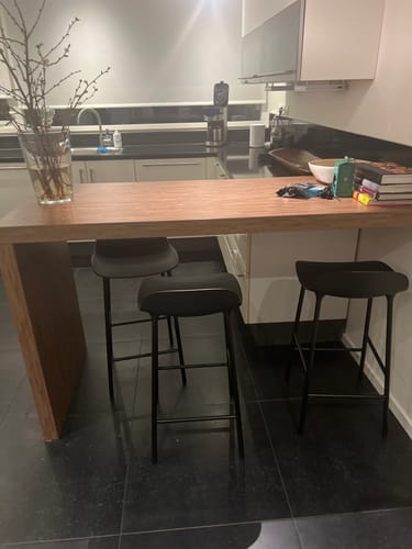 Klant toont de simpele, zwarte Normann Copenhagen Form barkrukken aan een houten keukeneiland.