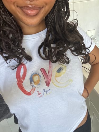 Close-up of a reviewer wearing the white love baby tee, highlighting the colorful front graphic.