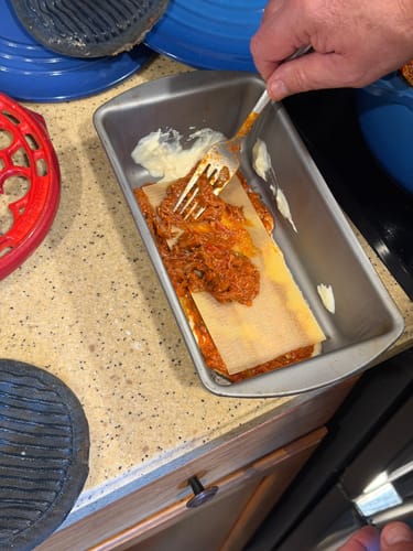 Reviewer layering lasagna in a loaf pan with a rich ragu made from USDA Choice Bone-In Short Ribs.