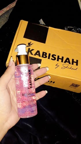 Customer holding a clear bottle of LuminaBright Whitening Face Wash, showing the pink gel, with the product box behind.