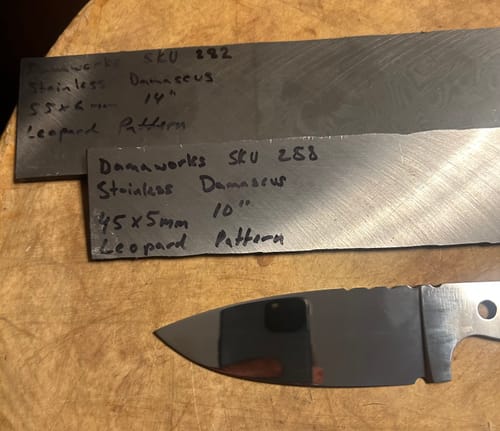 Close-up of a customer's shiny knife blade next to raw material, shaped with the sanding belt.