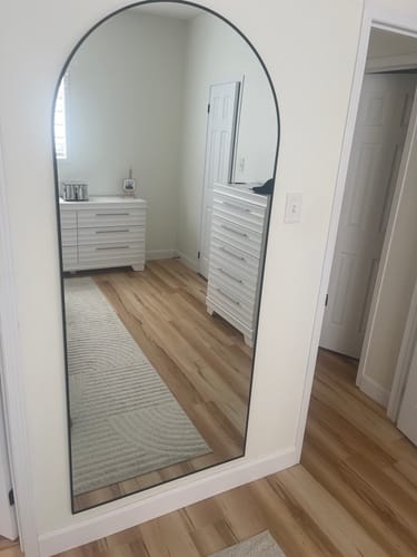 Reviewer's Black Full Length Arch Mirror leaning against a white wall in a bedroom setting.