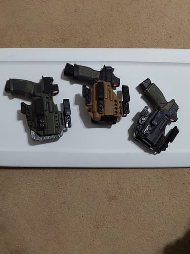 Customer's three XIPHOS ELITE holsters in green, tan, and black, laid out side-by-side with handguns fitted inside.
