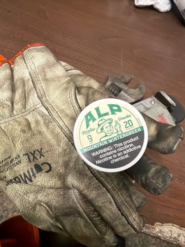 Customer's tin of Mountain Wintergreen Nicotine Pouches resting on a pair of worn work gloves.